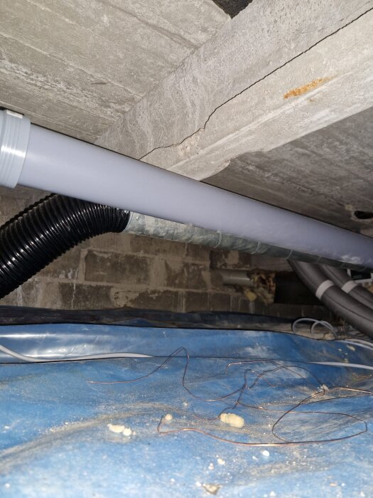 Spricka i betong i krypgrund med rör och ledningar där en lång spricka syns tydligt i materialet.