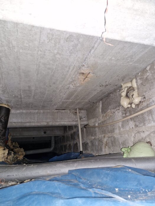 Spricka i krypgrundens betong med isolering och rör synliga.