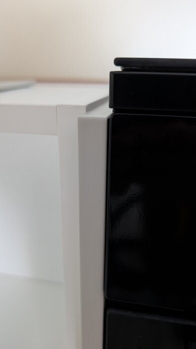 Närbild av vit sidopanel och svart skåpslucka i ett kök, där sidopanelen är en aning högre än luckan.