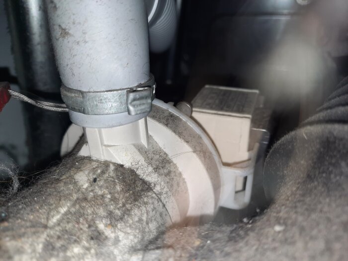 Grå slang med engångs-slangklämma monterad, omgiven av damm och maskindelar i en bygg- eller renoveringsmiljö.