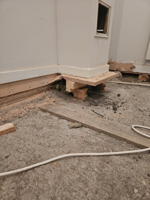 Inbyggd gipskanal med lös betong i botten, omgiven av trästöd och en öppen yta där betongen smular sönder. Kabel synlig på golvet.