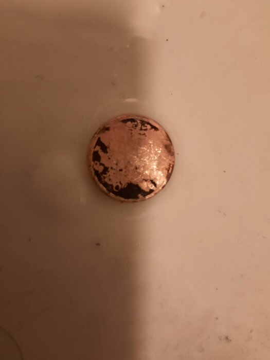 50-öring fast i mynningen i ett avlopp med vit bakgrund.