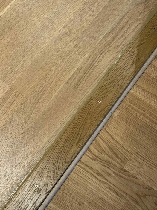 Träparkettgolv med fog och skruvar längs en skarv, färdigställd med vit golvfog för att förnya utseendet och förbättra finishen.