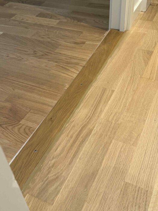 Golvsockel av trä med nylagd fog mellan två olika trägolv.