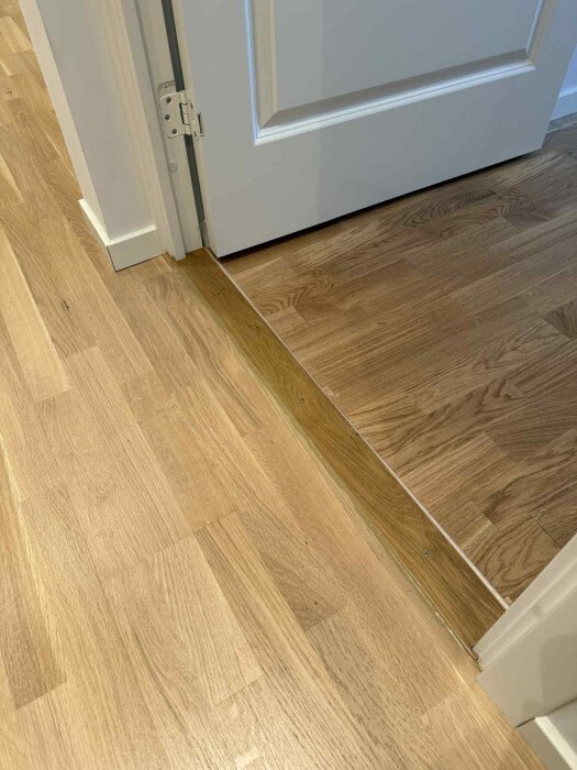 Trägolvskarv vid en dörröppning med nyanvänd vit golvfog för att förbättra utseendet mellan två golvytor.