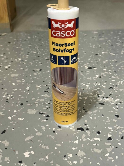 Förpackning av Casco FloorSeal Golvfog på grått fläckigt golv, 300 ml storlek använd för tätning av golvspringor.