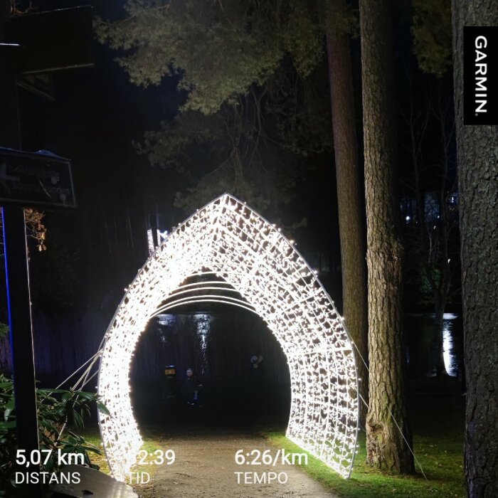 Ljusbåge i en park på natten, omgiven av träd. Texten visar distans 5,07 km, tid 32:39 och tempo 6:26/km.