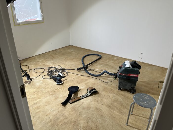 Verktyg och en dammsugare i ett rum med trägolv; förberedelser för att lägga foam och parkett.