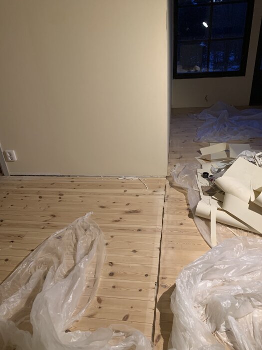 Skarv i innertak och golv där en vägg tidigare stått, omgivna av plast och borttagna materialrester i ett rum med trägolv och beige väggar.
