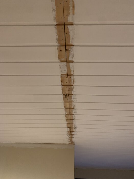 Skarv i innertak där en vägg tidigare funnits, med träbitar och spackel synliga mellan takpanelerna.