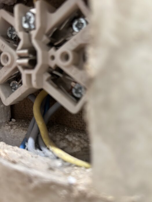 Eluttag öppnat från väggen med synliga ledningar och skruvar för koppling.