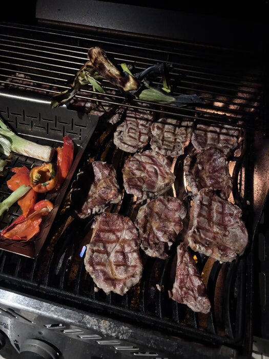 Grillad karré och grönsaker på en gasgrill med lågor, inklusive miniblomkål och paprikor.