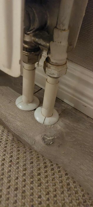 Radiatorrör kopplade till en värmeenhet ovanpå ett trägolv.