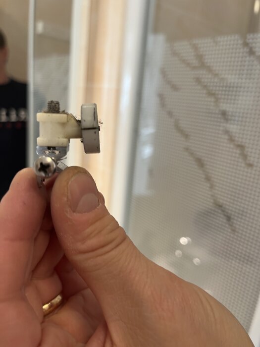 Hand som håller ett trasigt duschväggshjul i närbild, där den vita plastdelen har spruckit.