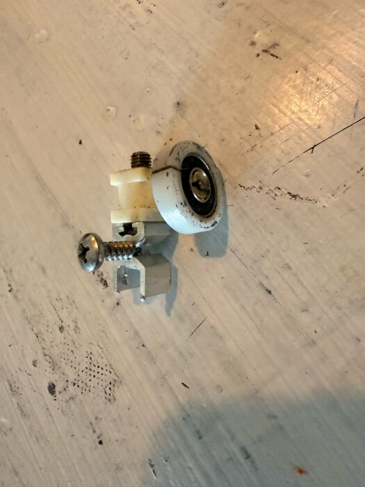 Duschväggshjul i metall och vit plast av, med skruv och mutter, del av skjutdörrssystem, på en träyta.