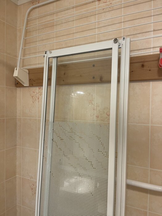 Duschvägg med hjul bland kaklade väggar; hjulen trasiga, behov av nya.