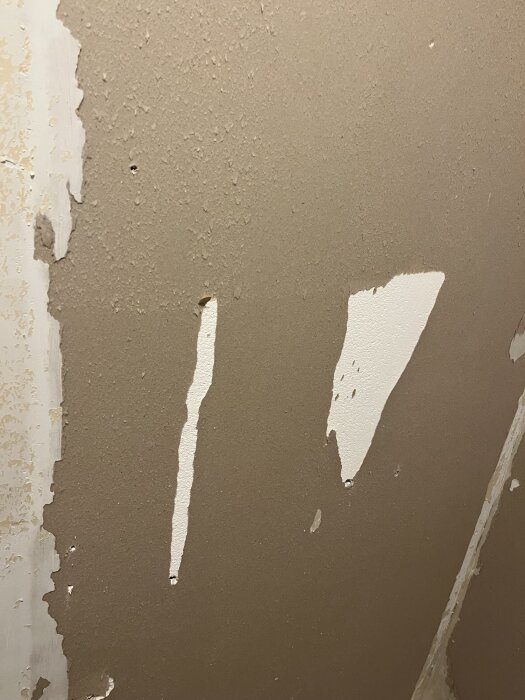 Gipsskiva i ett badrum under renovering, med synliga rester av lim och vit färg.