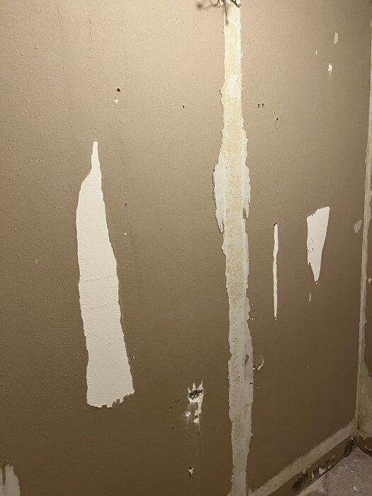 Gipsvägg efter att plastmatta tagits bort, visar gamla spikhål och limrester, i samband med badrumsrenovering.
