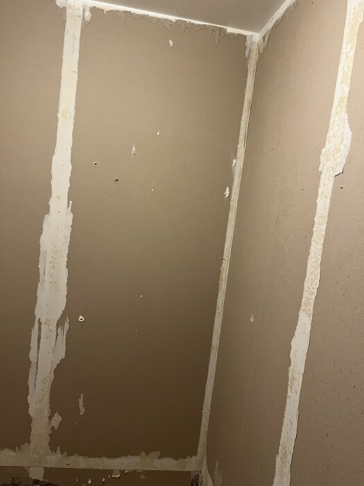 Väggar i ett renoverat badrum med synligt gips, där plastmatta har tagits bort. Gipsen är limmad och spikad, med rester av lim och spikhål.