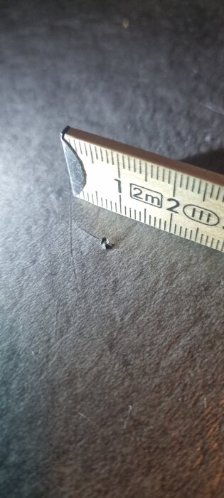 Knappnålsstort hål och ytlig repa i våtrumsmatta, uppmätta med linjal.