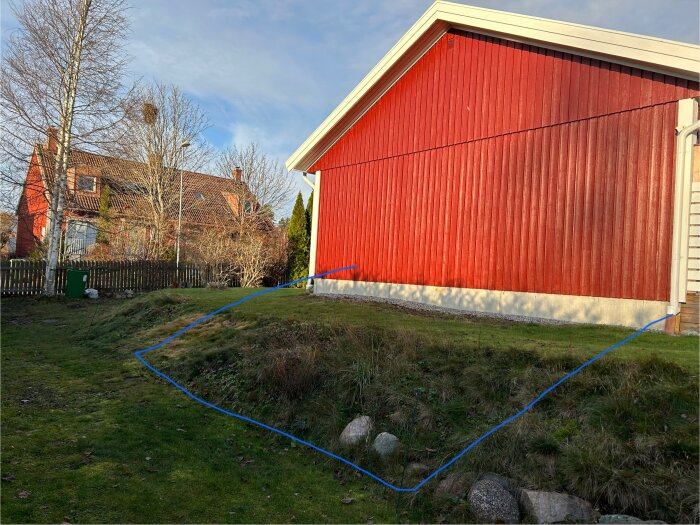 Röd villa med synlig grund och grässlänt, blå ruta markerar planerad tillbyggnad.