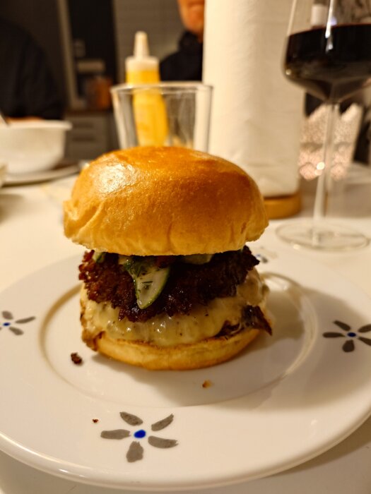 Hamburgare i briochebröd med pepperjackost, bacon och dillpicklad gurka, serverad på en tallrik.
