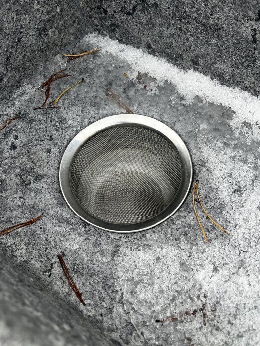 Rostfri sil insatt i ett avlopp omgiven av snö och is, där handtaget har tagits bort.