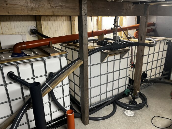 Två balanstankar anslutna med stora 110 mm rör för snabbare utjämning, placerade i en träkonstruktion inomhus.