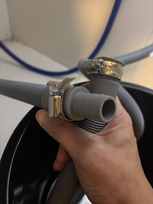 Hand håller i två grå slangar som är kopplade med metallslangklämmor, vilket orsakar läckageproblem med tvättmaskinsanslutningen.