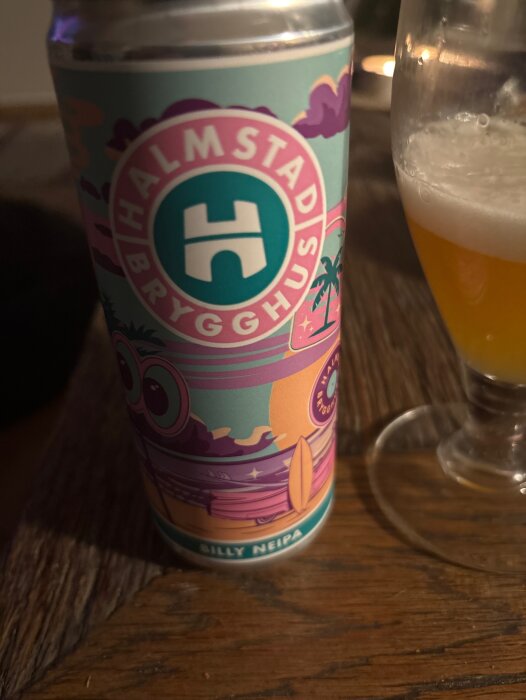 Burk med Halmstad Brygghus NEIPA och ett halvfullt glas öl på ett träbord.