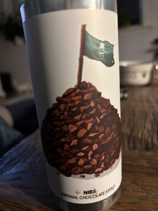 En burk Nibs Imperial Chocolate Stout med etikett av chokladbitar och en flagga på en träyta.