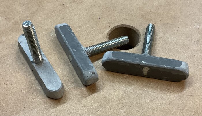 Tre laxstjärtspårmojänger i epoxi med monterade M6-skruvar på en arbetsbänk.