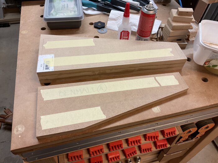 Träblock med maskeringstejp på arbetsbänk, förberedda för sågning. Verktyg och material runt omkring.