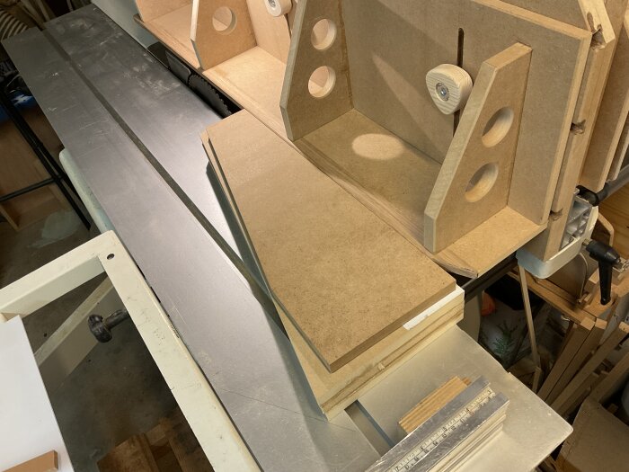 Träverkstad med bordssåg och hög anhållsinstallation, omgiven av MDF-skivor och arbetsverktyg, redo för formtillverkning av bordsben.