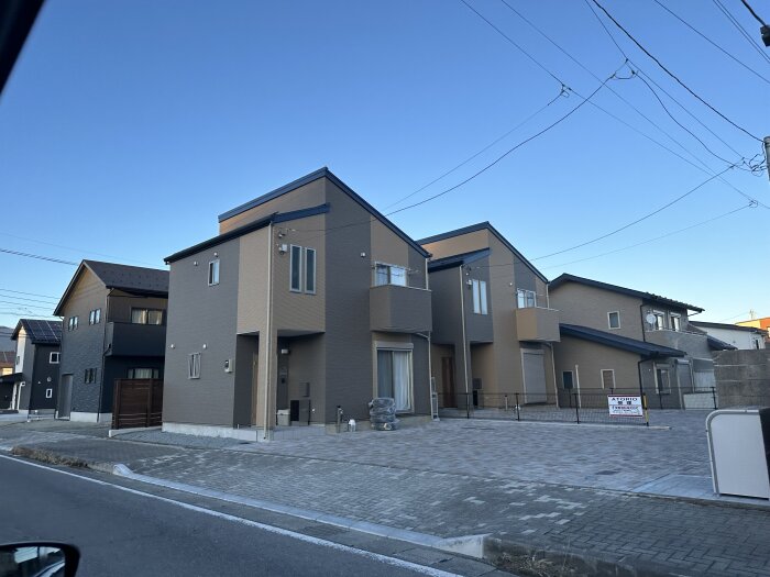 Nybyggda moderna hus i Japan med brun och grå fasad, fotograferade på en gata under en klarblå himmel.