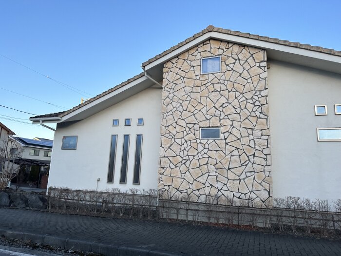 Nybyggt hus i Japan med vit fasad och dekorativ stenpanel, stora vertikala fönster och ett valmat tak.