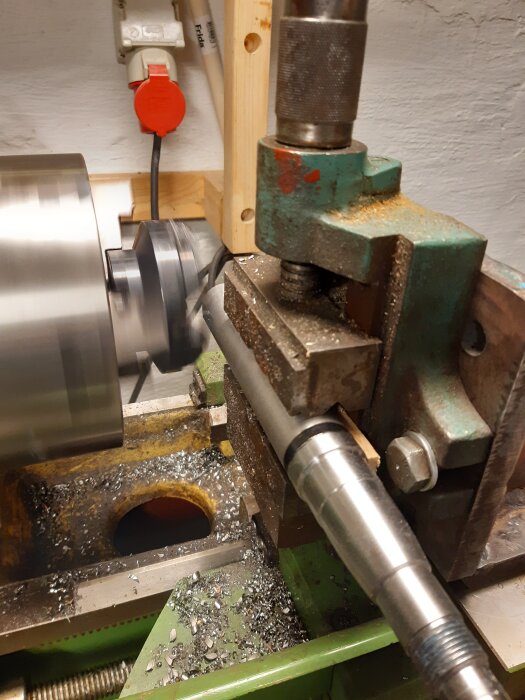 Svarv ombyggd till fräs för bearbetning, metallspån på bänken. Verktyg och maskindel i fokus i ett trångt arbetsutrymme.