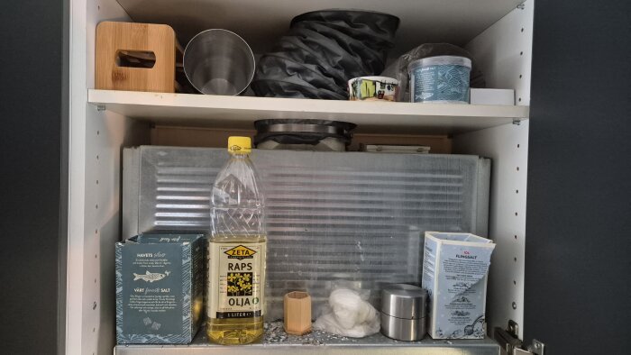 Överskåp med köksfläkt, rapsolja och diverse köksprodukter; synlig ventilation utan kallrasskydd, försök till tätning med tejp för att minska kalldrag.