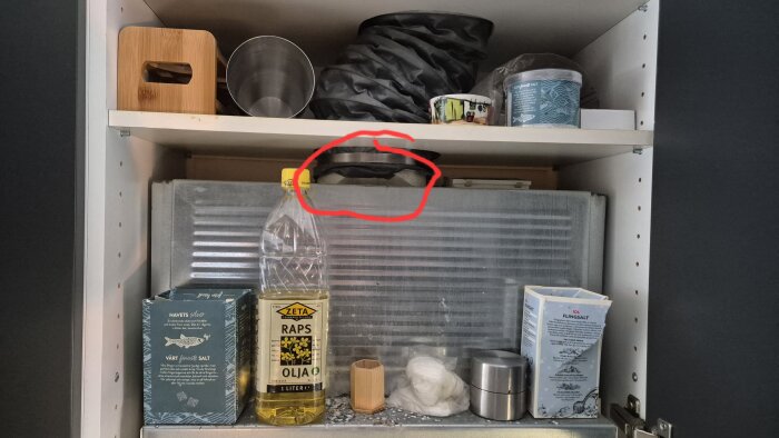 Köksskåp med rödmarkerat område kring kallrasskydd ovanför köksventilation, omgiven av flaska rapsolja, salt och andra köksartiklar.