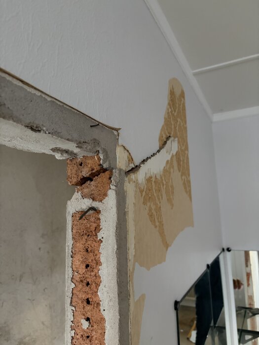 Sprucken vägg av lättbetong i lägenhet under renovering, med borttaget garderobsspår och blottad orangefärgad tegelhålsten.