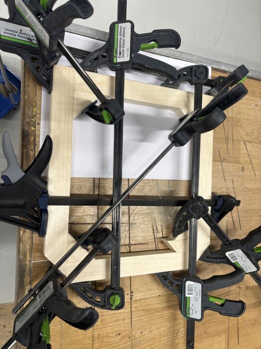 Träram för fönster sitter fastspänd med flera tvingar på en arbetsbänk under konstruktion.