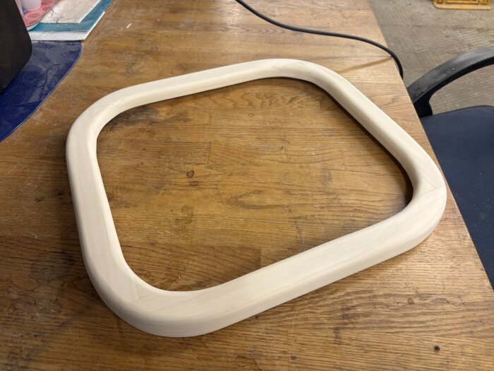 Handgjord fönsterram i trä liggande på ett arbetsbord av trä. Ramen har rundade hörn och är noggrant slipad för en jämn finish.