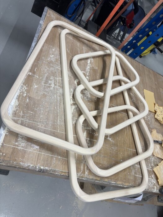 Hantverksskurna fönsterramar av ljust trä ligger på ett arbetsbord i en verkstadsmiljö, redo för montering.