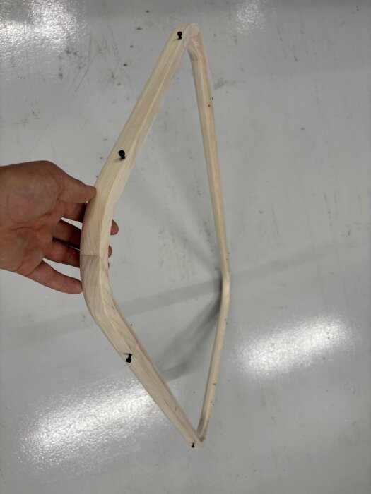 Träram för fönster med skruvhål syns mot bakgrund av ett ljust golv. En hand håller ramen, visar dess struktur och form.