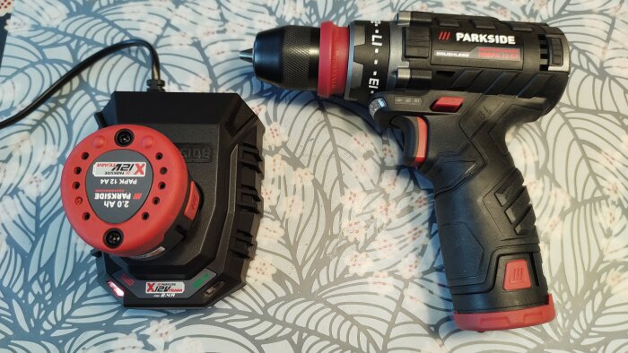 Parkside 12V borrskruvdragare med tillhörande batteri och laddare placerade på ett mönstrat bord.