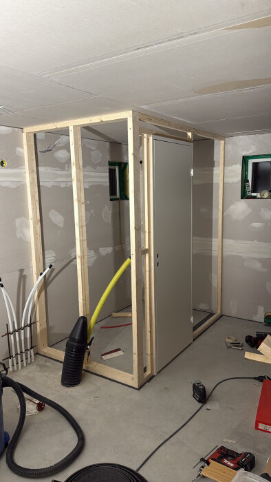 Träram för väggkonstruktion med dörr monterad, omgiven av verktyg och material i ett pågående byggprojekt.