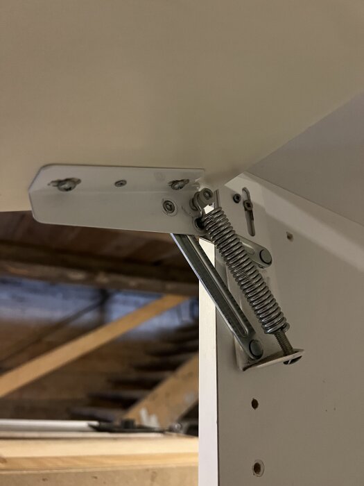 Inre del av ett skåp med ett gångjärn och en fjädermekanism, potentiellt från Ballingslöv, synlig i en verkstadsmiljö.