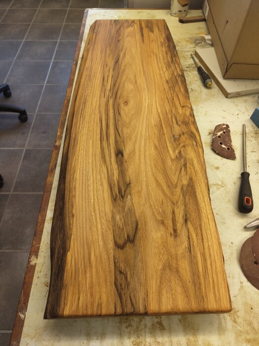 Handgjord träskärbräda/uppläggningsbricka av återvunnet trä, liggande på ett arbetsbord med verktyg i bakgrunden.