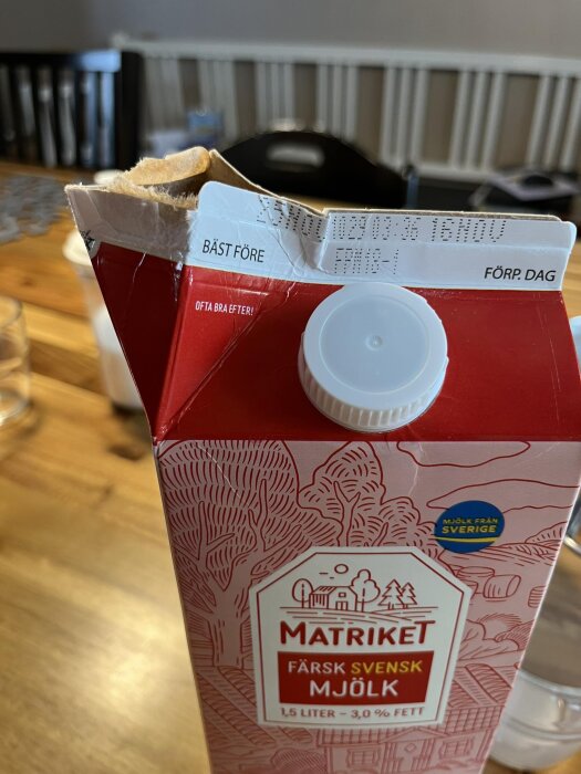 Öppnad mjölkförpackning i kartong med plastskruvkork, datum synligt på fliken, diskussion om plastkomponentens syfte.