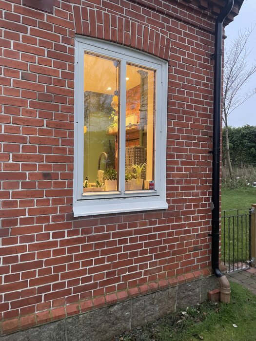 Ett tegelfasad med ett nyrenoverat fönster. Garderoben syns i inredningen genom fönstret.